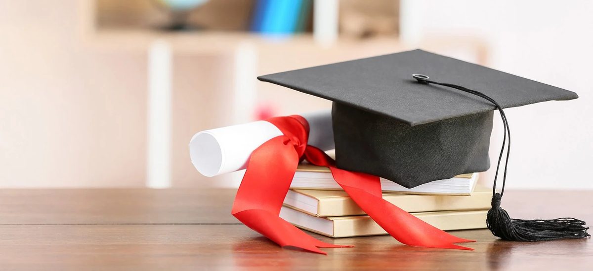 A graduation cap and diploma resting on a stack of books