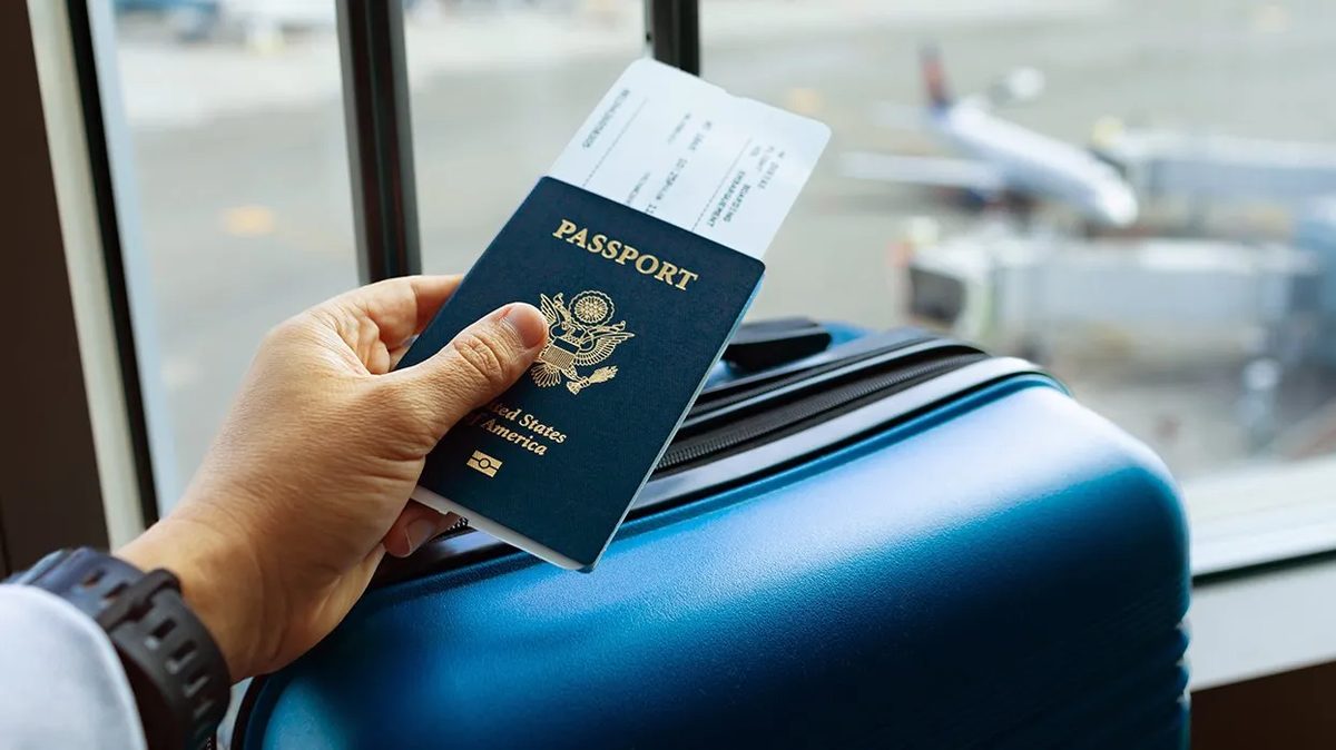 A student holding a passport and boarding pass in front of an airport window